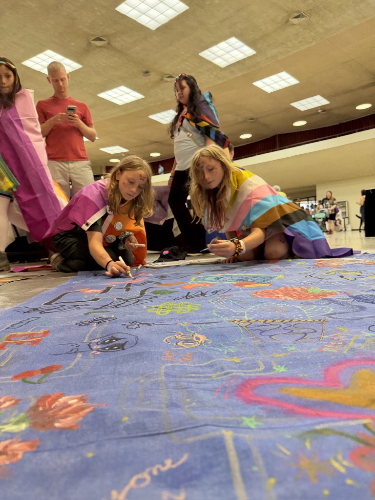 Youth painting a blue Surface/Self canvas under Pride flags.
